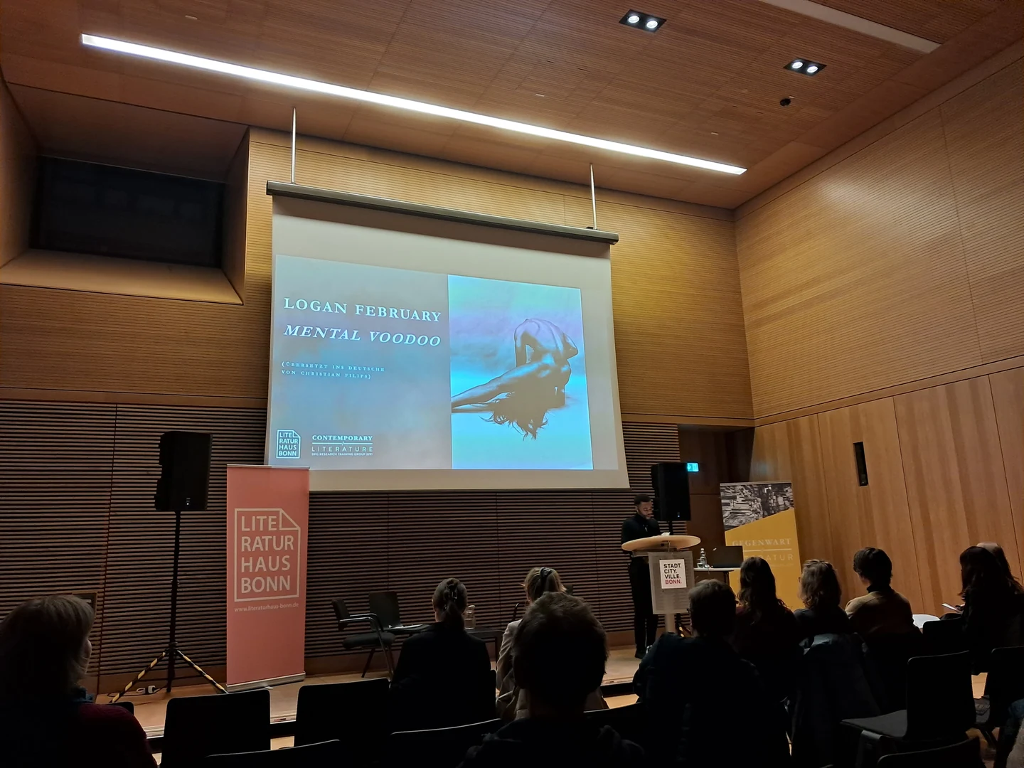 Eine Wissenschaftlerin und ein Wissenschaftler arbeiten hinter einer Glasfassade und mischen Chemikalien mit Großgeräten.