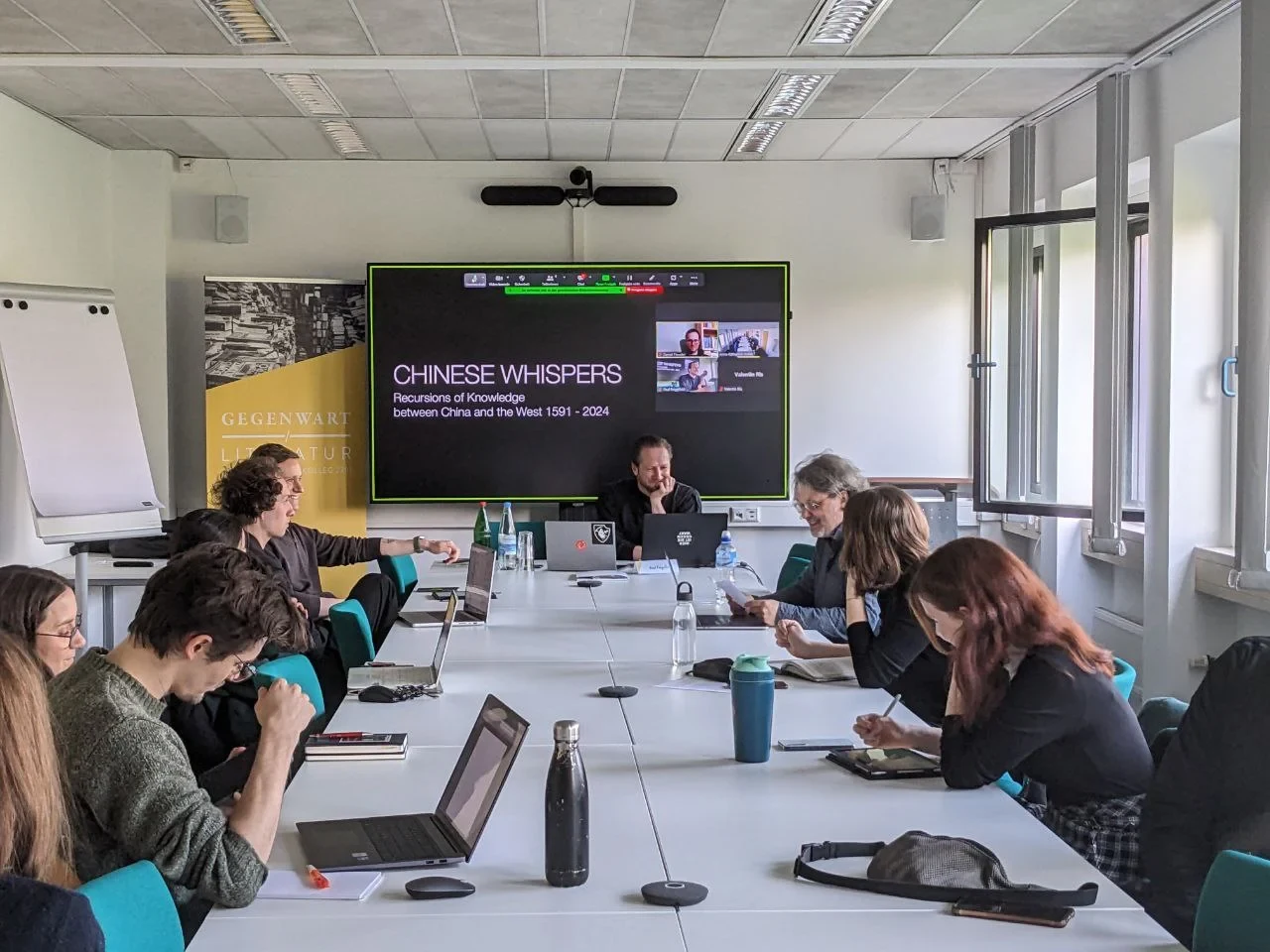 Eine Wissenschaftlerin und ein Wissenschaftler arbeiten hinter einer Glasfassade und mischen Chemikalien mit Großgeräten.