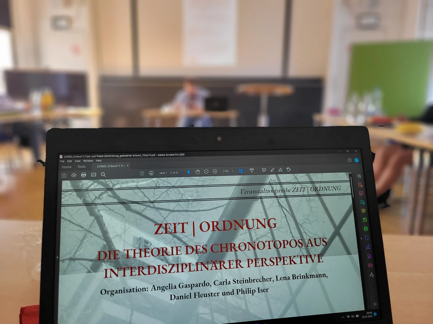 Eine Wissenschaftlerin und ein Wissenschaftler arbeiten hinter einer Glasfassade und mischen Chemikalien mit Großgeräten.